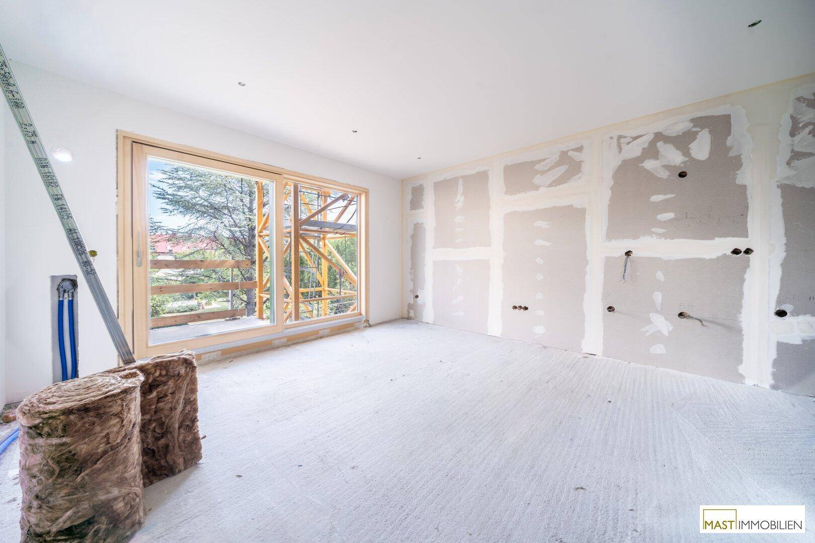 Unfertiger Innenraum im Rohbau mit großen Schiebetüren und Blick auf die Baustelle.