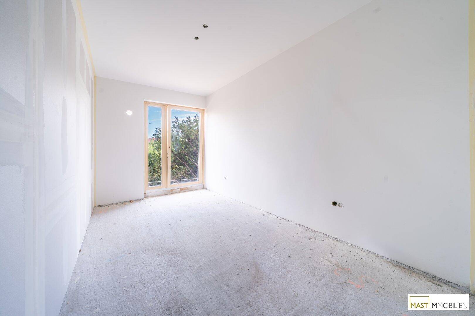 Heller, unfertiger Raum mit einer einzelnen Fenstertür, die Zugang nach draußen ermöglicht.