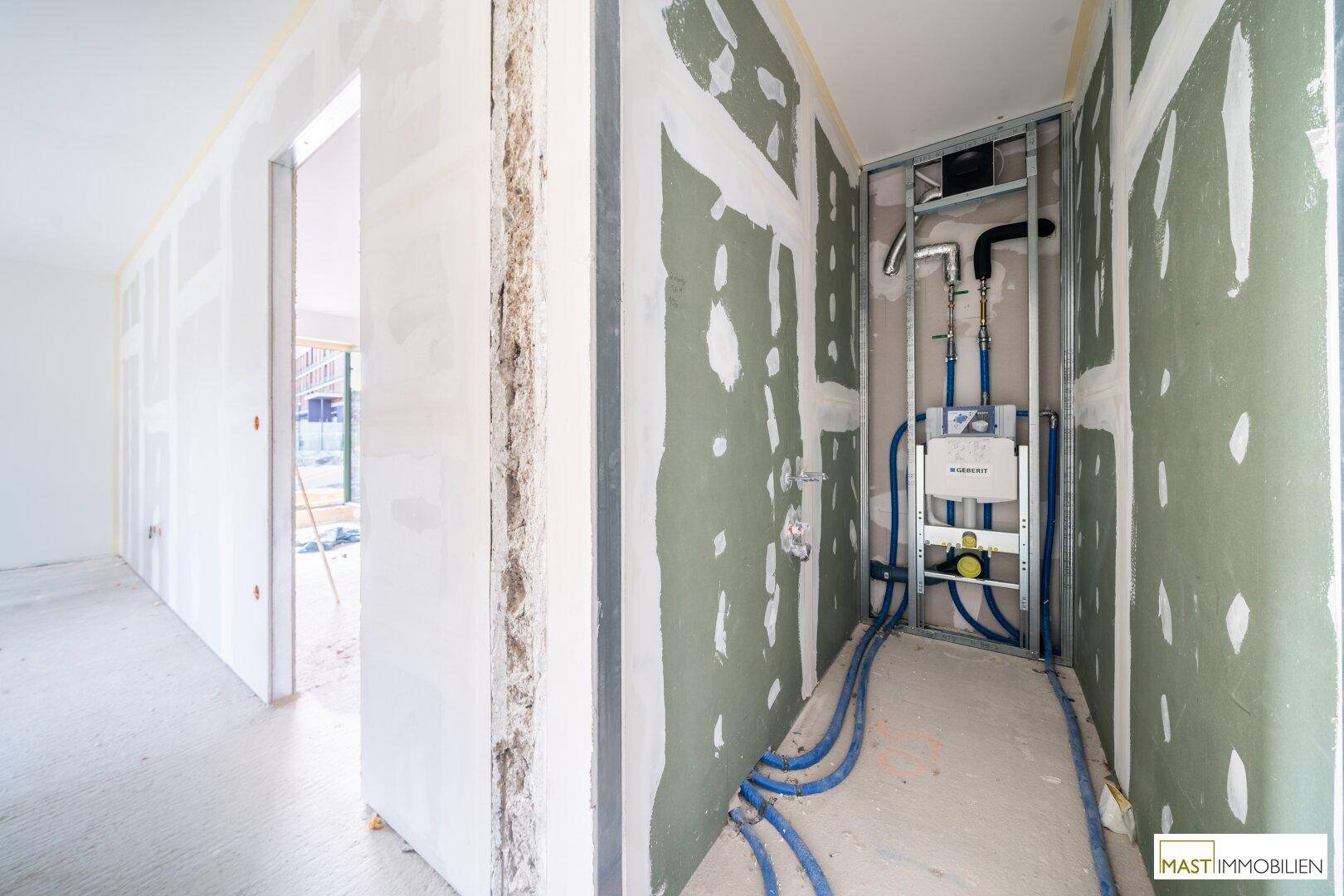 Unfertiger Badezimmerbereich mit sichtbaren Sanitärinstallationen und Trockenbauwänden im Rohbauzustand.
