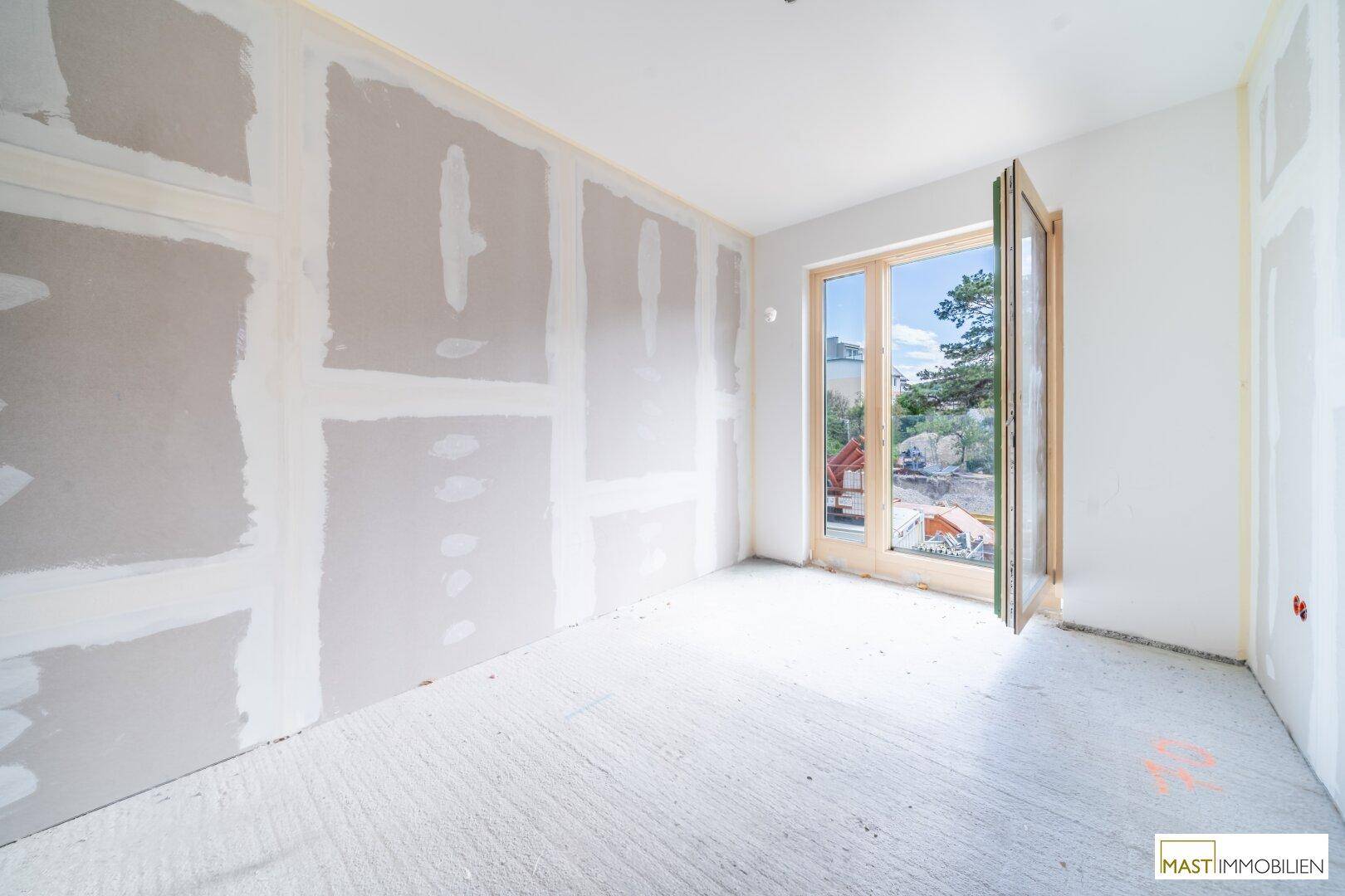 Unfertiger Raum mit Trockenbauwänden und einer geöffneten Fenstertür, die frische Luft hereinlässt.