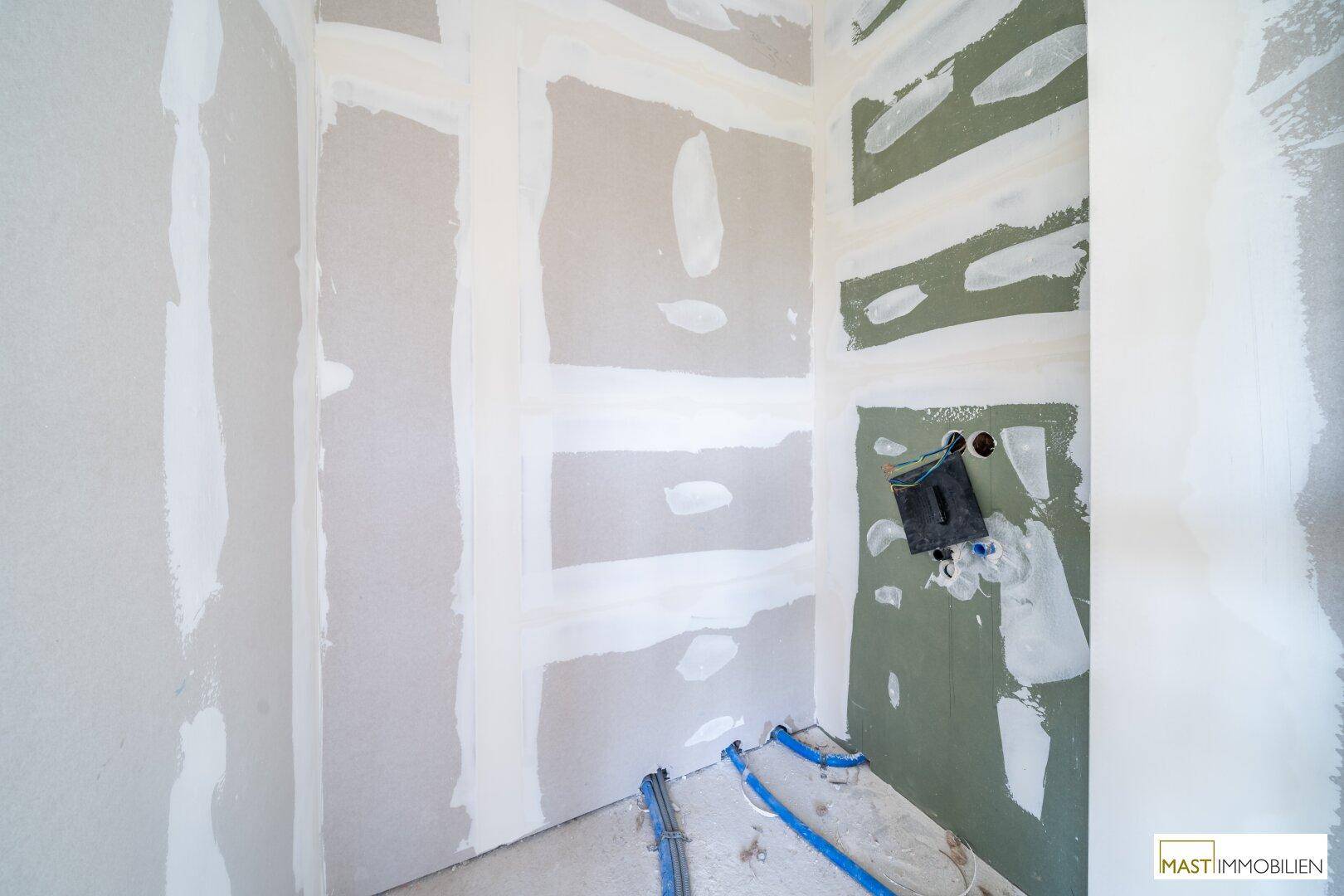 Unfertiges Badezimmer mit Trockenbauwänden und vorbereiteten Anschlüssen für Sanitärinstallationen.