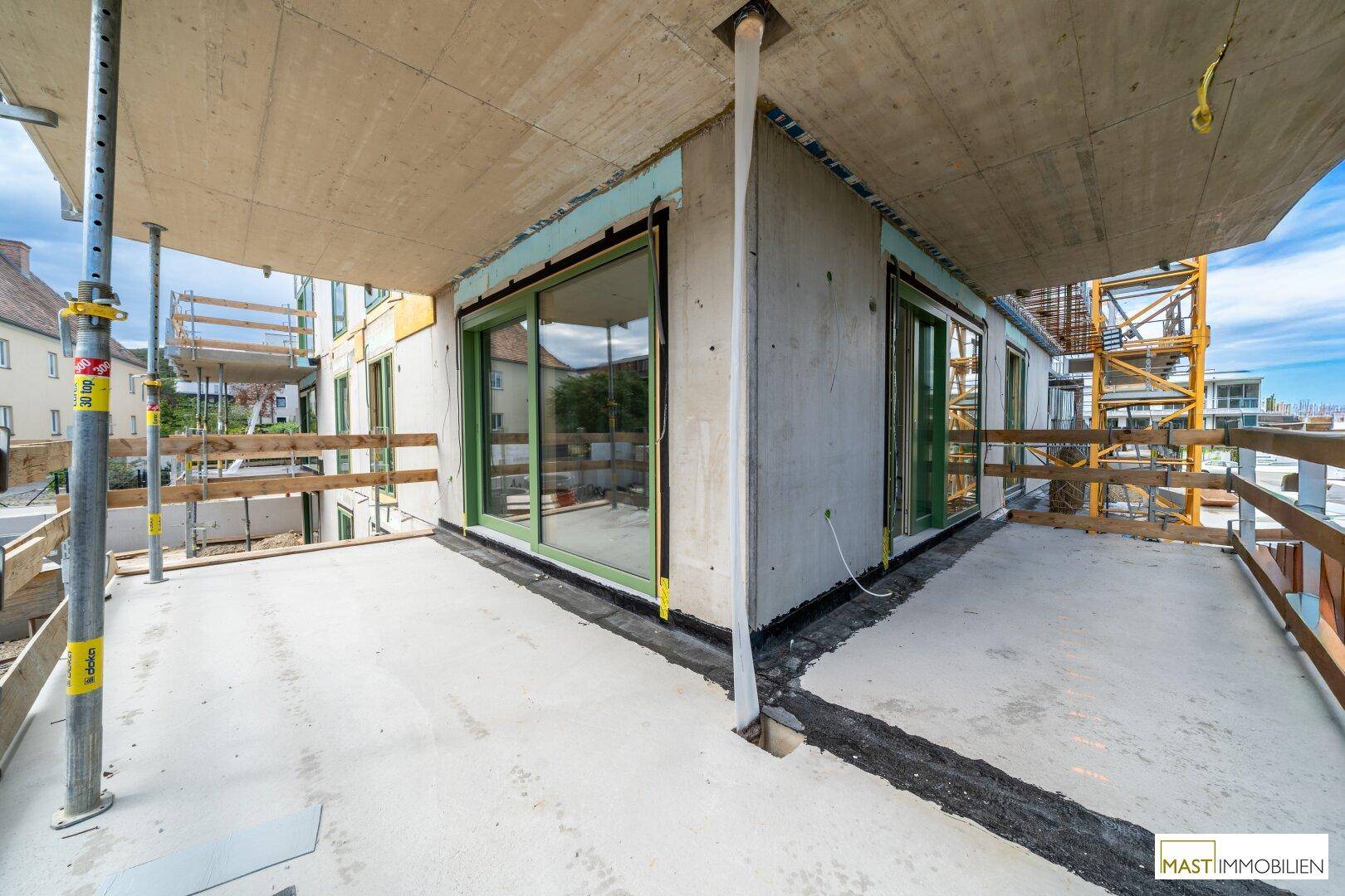 Große, unfertige Terrasse im Rohbau mit Blick auf die Umgebung und Baustellenelemente.
