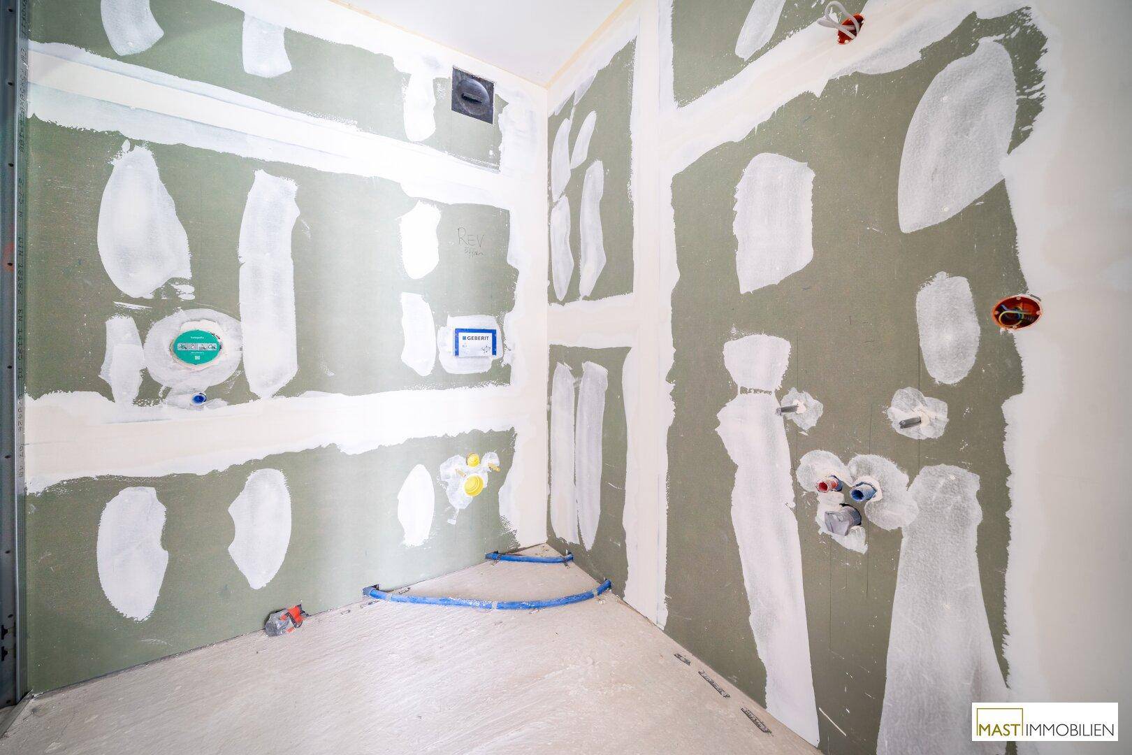 Rohbaubadezimmer mit Installationen für Dusche, Toilette und Waschbecken.