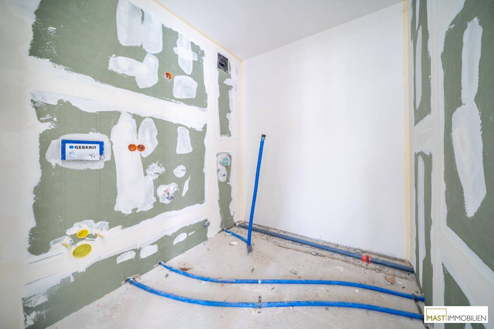 Badezimmer im Rohbau mit vorbereiteten Anschlüssen für Toilette und Waschbecken.