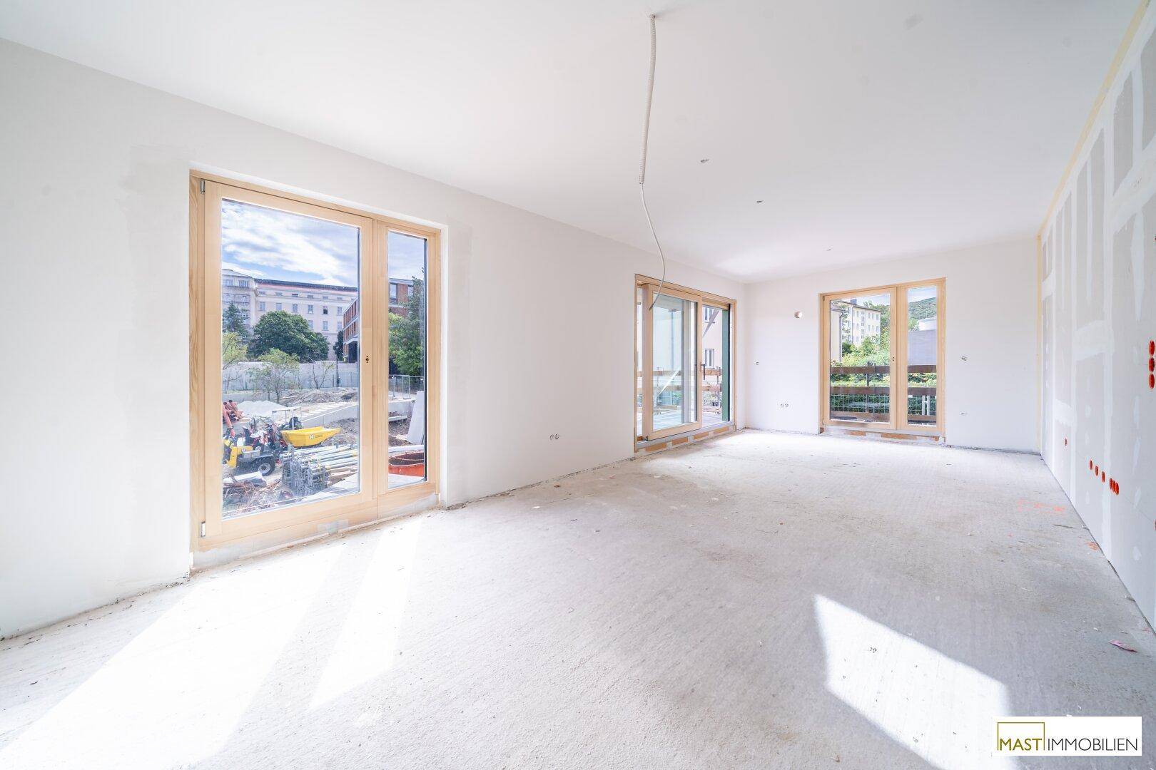 Helles Zimmer im Rohbau mit großen Fenstern und Blick auf die Baustelle.