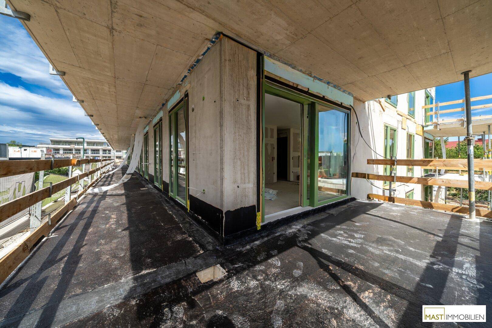 Große, unfertige Terrasse im Rohbau mit Blick auf die umliegende Baustelle.