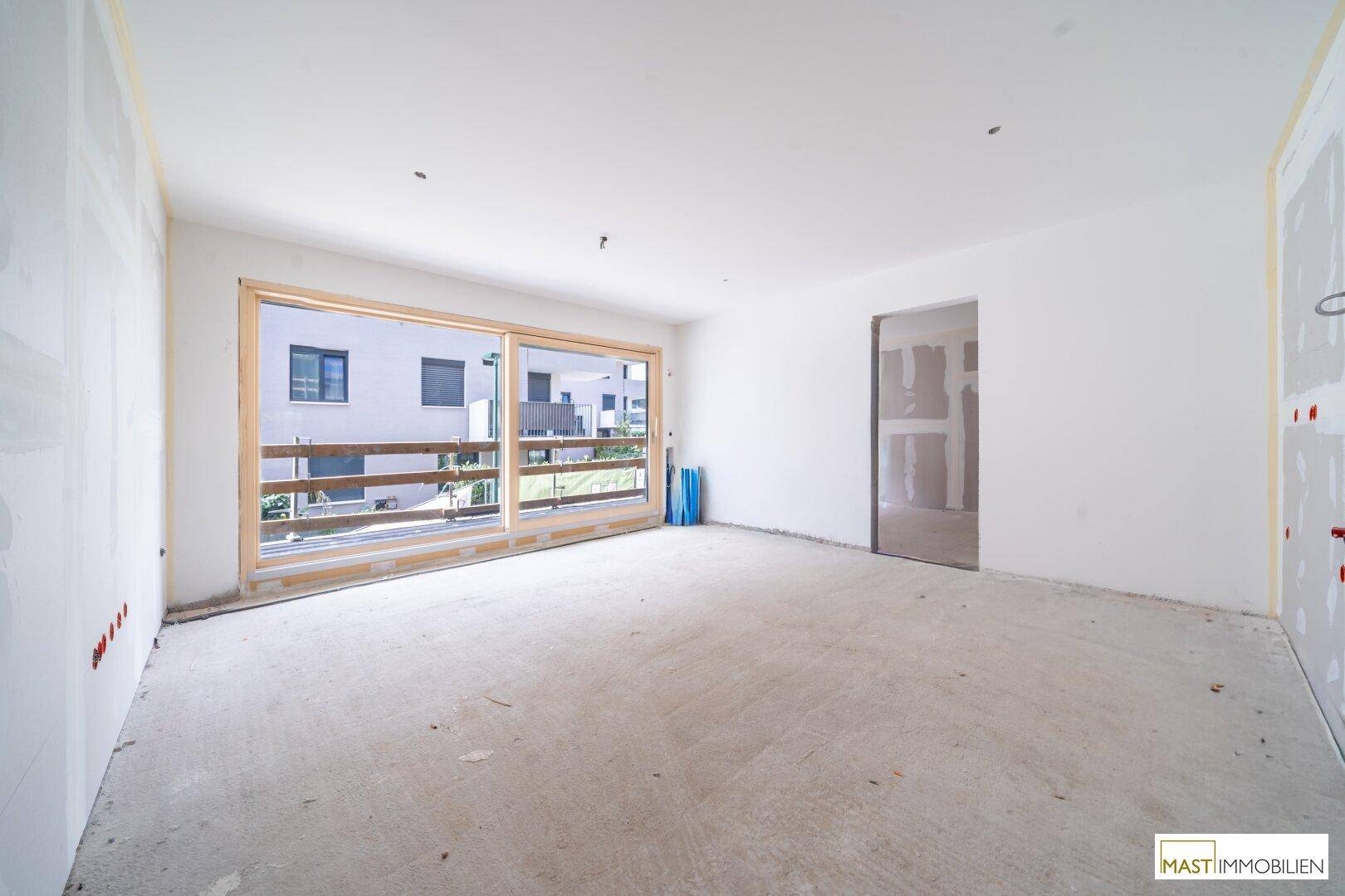 Unfertiger Innenraum mit großen Fenstern, Rohbauwänden und Betonboden, bereit für den Ausbau.