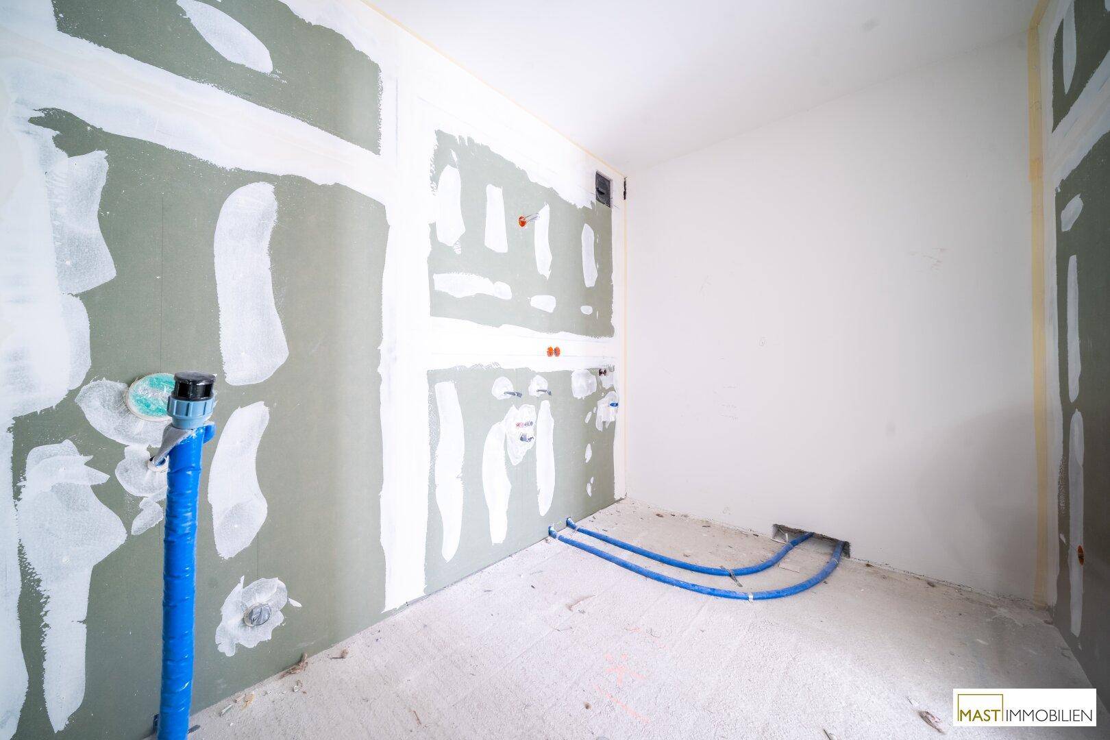 Rohbau eines Badezimmers mit sichtbaren Wasserleitungen und Trockenbauwänden, bereit für die Installation.