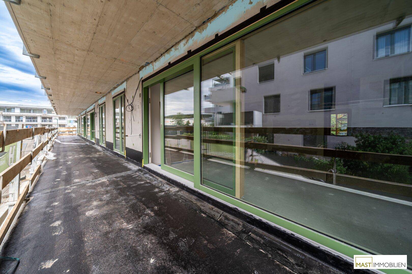 Langer Balkon im Rohbau mit großen Glasschiebetüren und Blick auf die Umgebung.