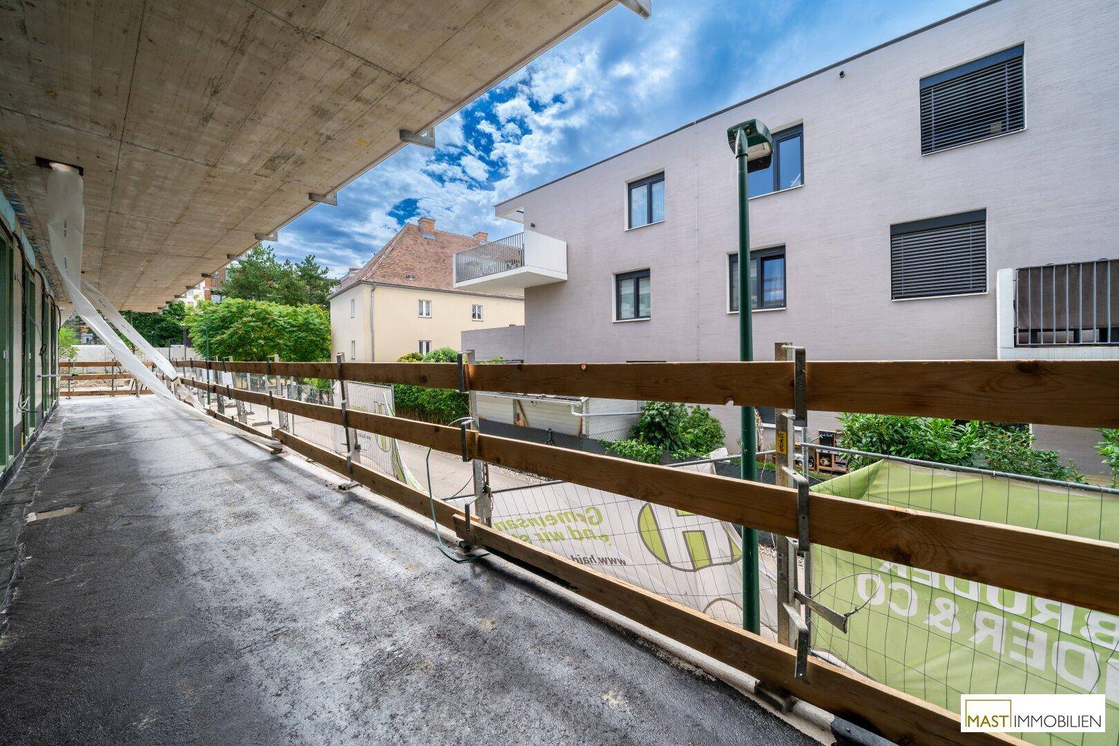 Langer Balkon im Rohbau mit temporärem Geländer und Blick auf umliegende Gebäude.