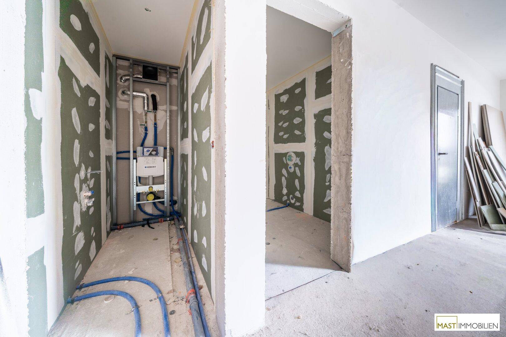 Badezimmer im Rohbau mit installierten Sanitärrohren und grünen Trockenbauplatten.