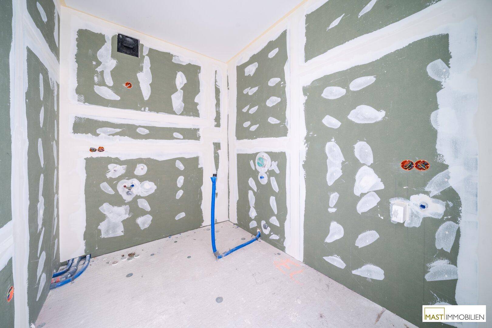 Unfertiges Badezimmer mit vorbereiteten Anschlüssen für Sanitär und Elektrik.