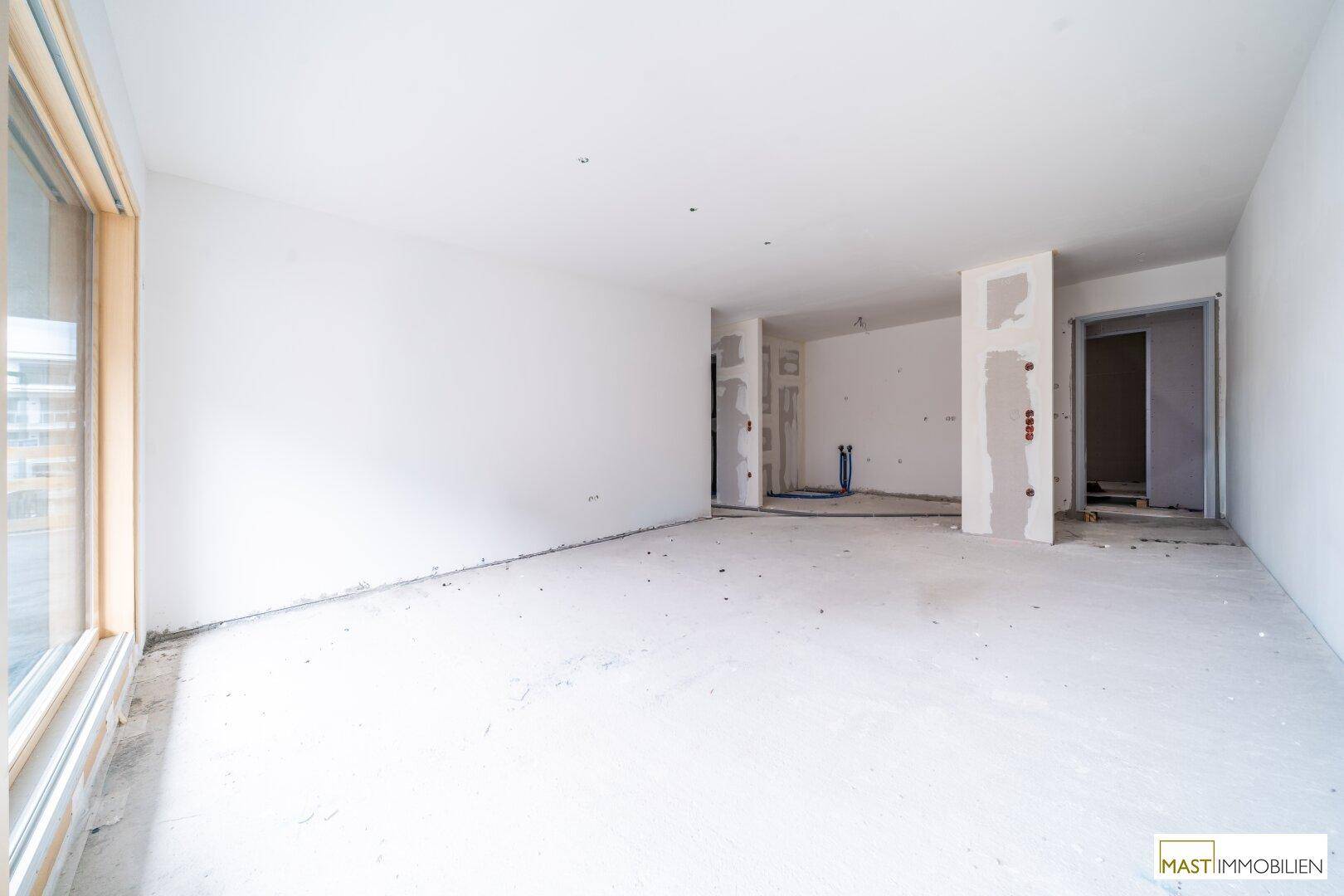 Heller Rohbau-Innenraum mit großen Fenstern und vorbereiteten Wänden für den weiteren Ausbau.