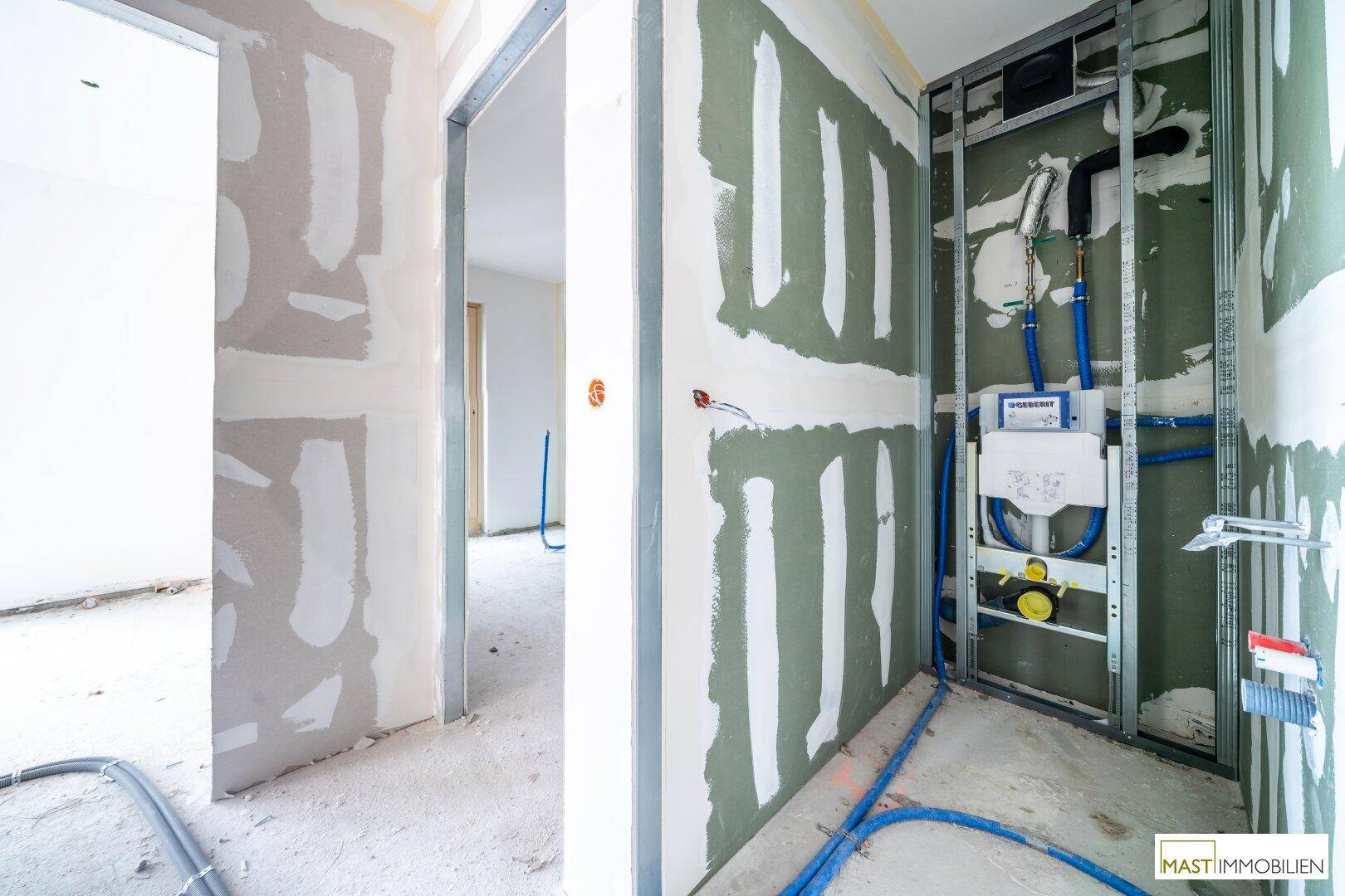 Rohbau-Badezimmer mit sichtbaren Installationen für eine Wandtoilette und vorbereiteten Wänden.