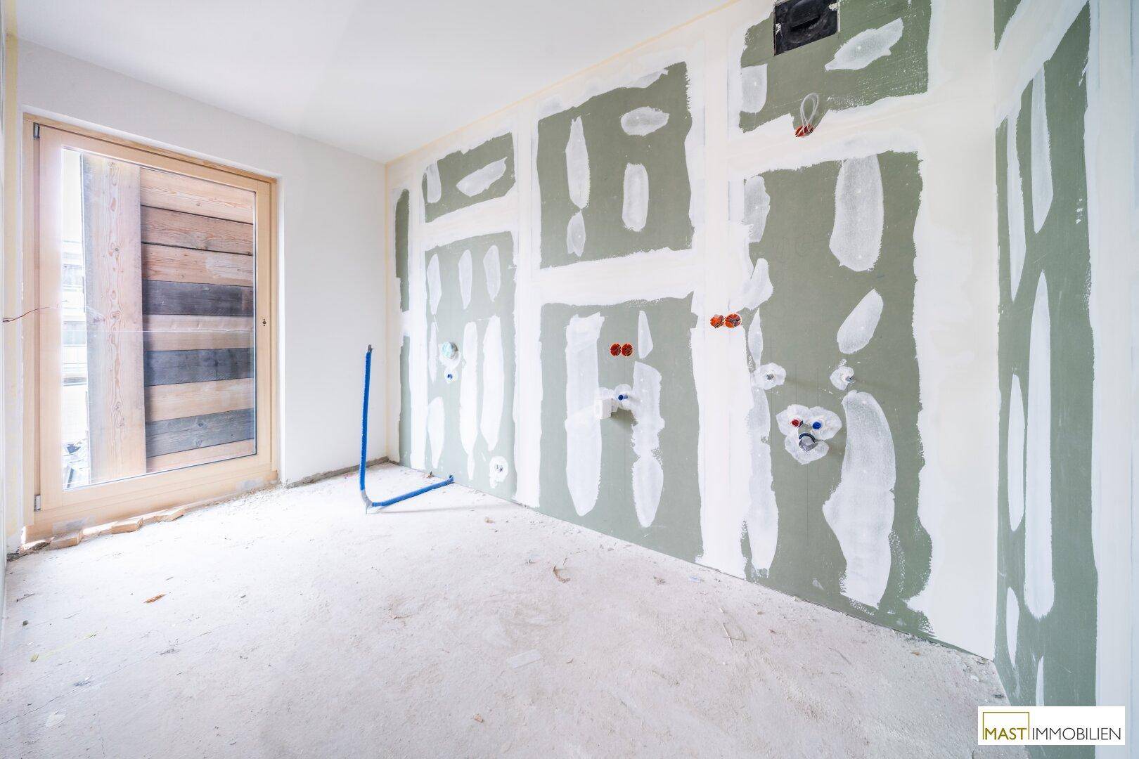 Rohbauzimmer mit sichtbaren Sanitärinstallationen und Holztür, bereit für den finalen Ausbau.