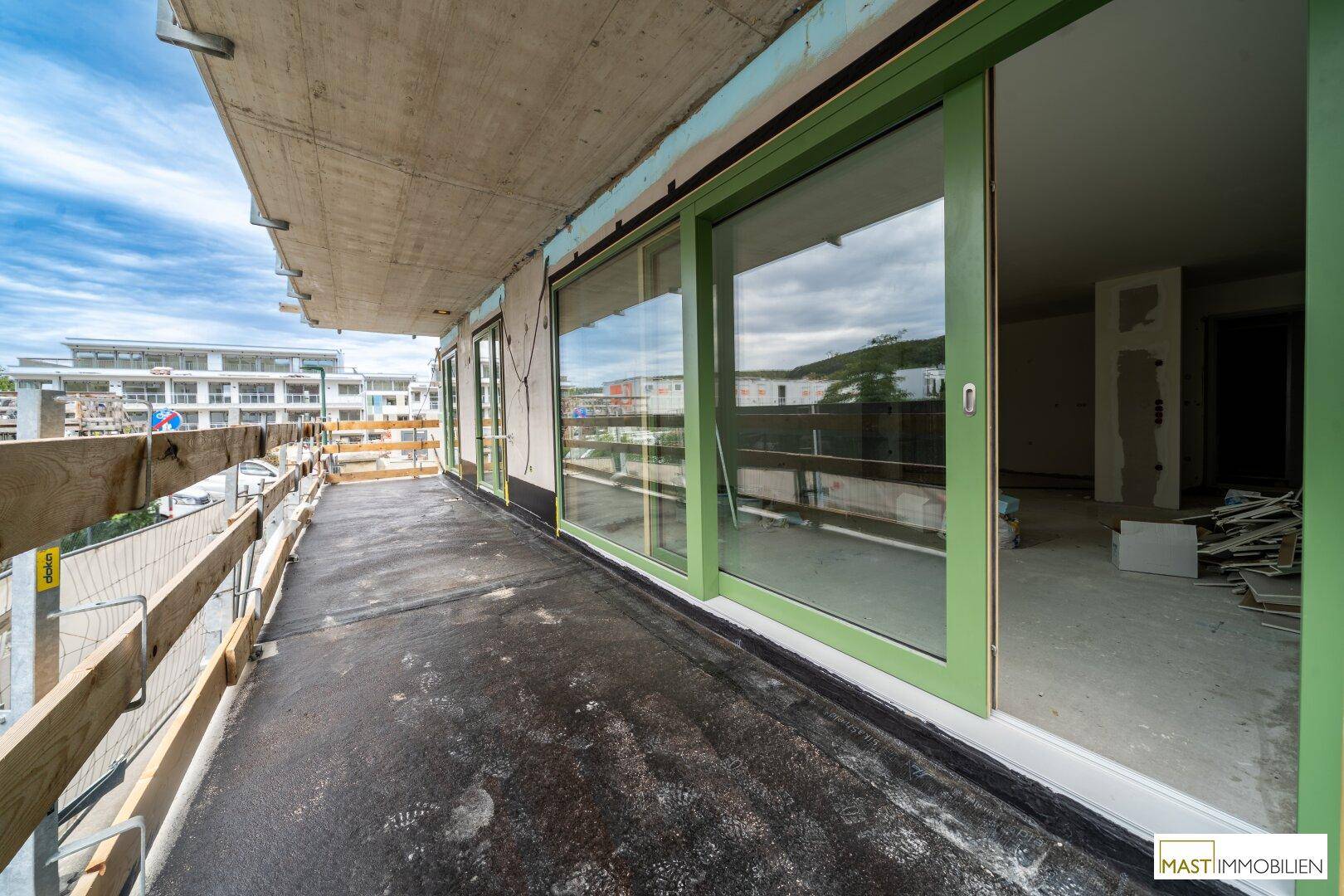Balkon im Rohbau mit grünen Schiebetüren und Blick auf die umliegende Bebauung.