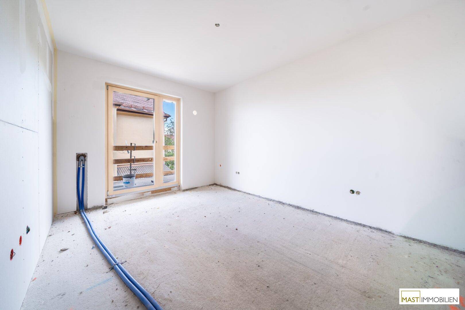 Unfertiges Zimmer mit Zugang zu einem kleinen Balkon und sichtbaren Installationen am Boden.