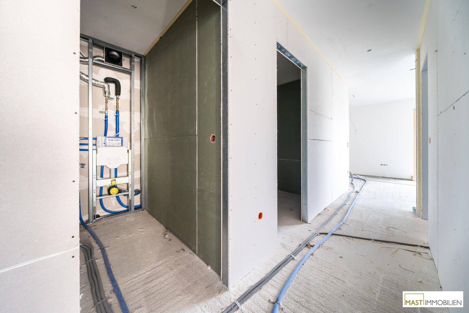 Rohbau-Flur mit Installationen für ein WC und Trockenbauwänden im Bauzustand.