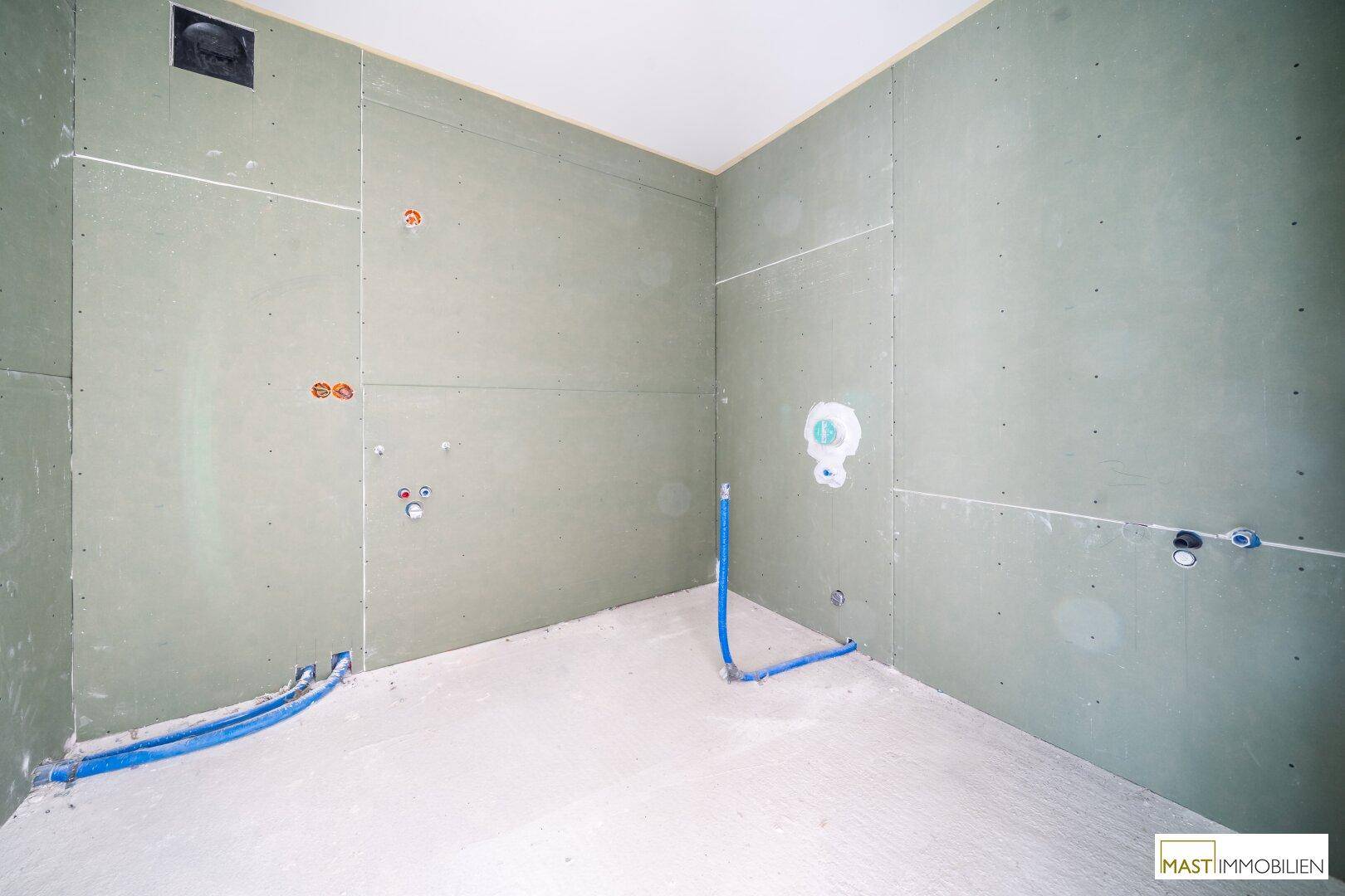 Unfertiges Badezimmer mit grünen Trockenbauwänden und sichtbaren Wasseranschlüssen für Sanitärobjekte.