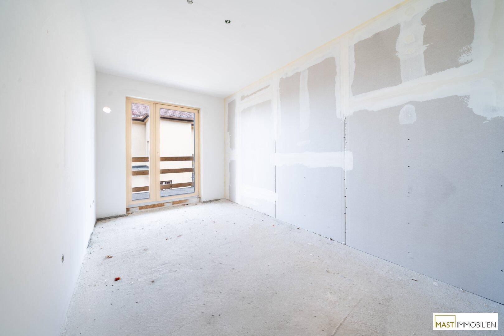Rohbau-Zimmer mit Trockenbauwänden und Fenster, das viel natürliches Licht hereinlässt.