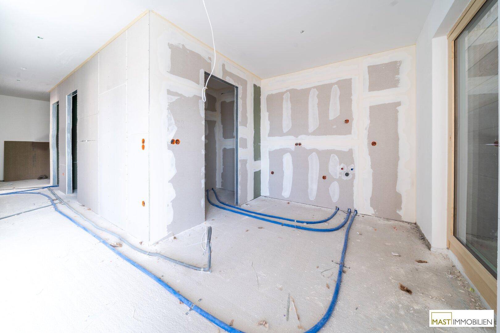 Rohbau-Innenraum mit Trockenbauwänden, sichtbaren Leitungen und Türöffnungen während der Bauphase.