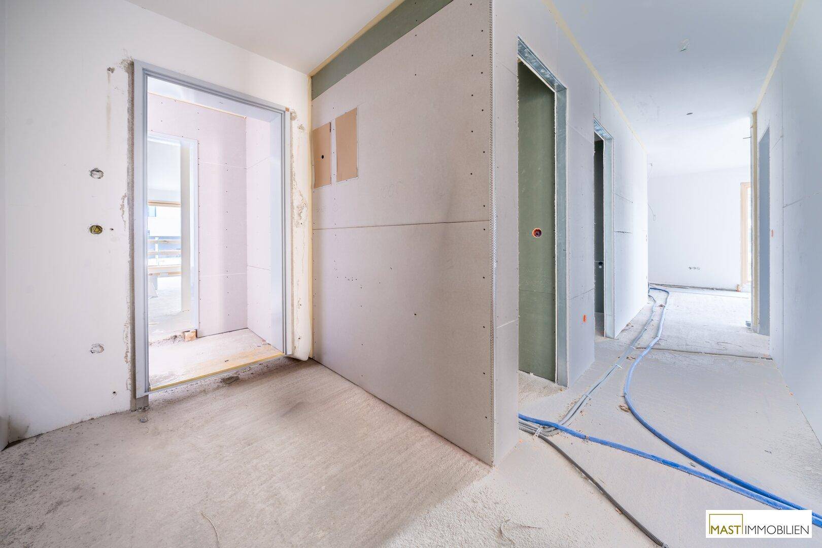Unfertiger Flurbereich mit Trockenbauwänden, Türöffnungen und sichtbaren Installationsleitungen.