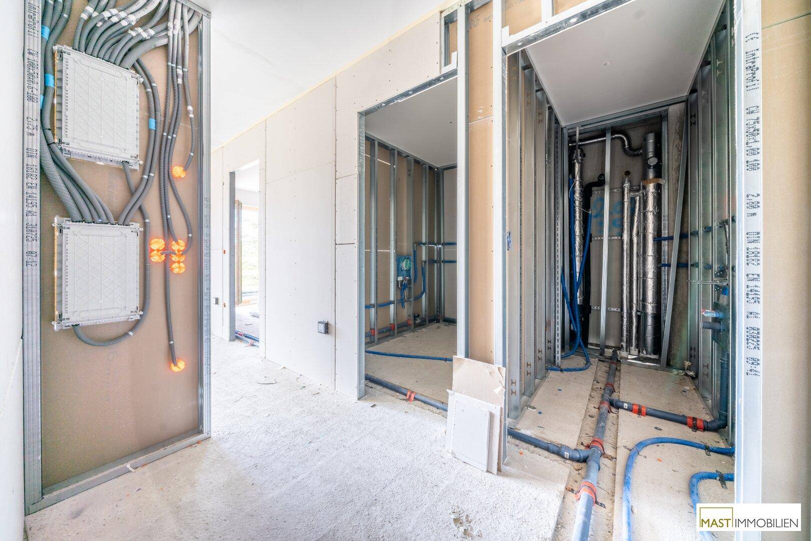 Rohbau eines Flurs mit umfangreichen Elektro- und Sanitärinstallationen sowie Metallständerwerk.