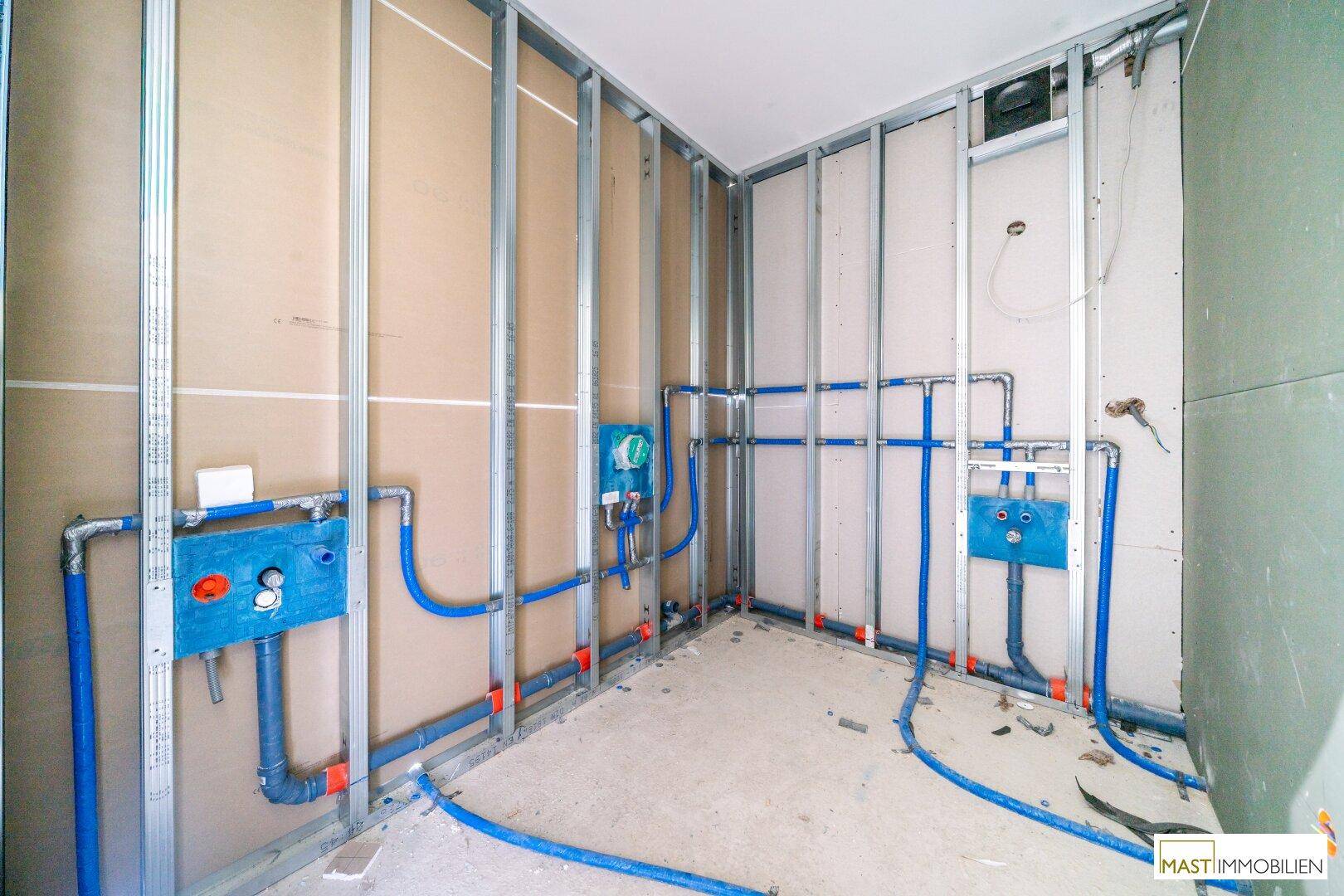 Badezimmer im Rohbau mit vorbereiteten Anschlüssen für Sanitäranlagen und Metallständerwerk.