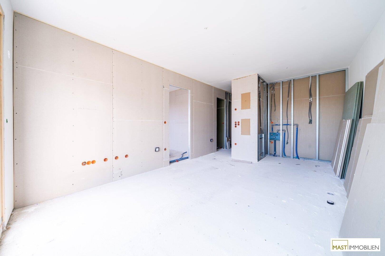 Innenraum im Rohbau mit Trockenbauwänden und sichtbaren Installationen für Elektrik und Sanitär.
