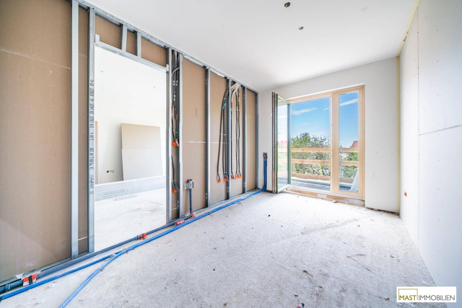 Rohbau eines Zimmers mit Metallständerwerk, sichtbaren Leitungen und Zugang zu einem Außenbereich.