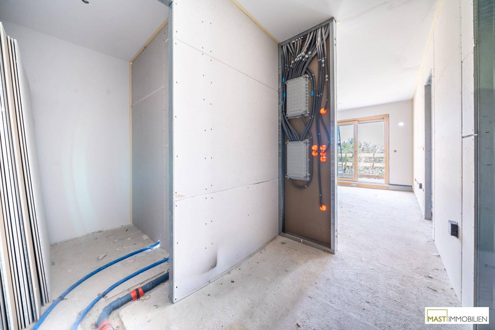 Flurbereich im Rohbau mit sichtbaren Elektroinstallationen und Trockenbauwänden, bereit für den Innenausbau.