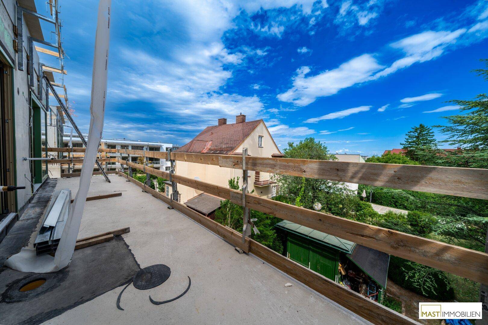 Unfertiger Balkon mit provisorischem Geländer und Blick auf umliegende Gebäude und Bäume.