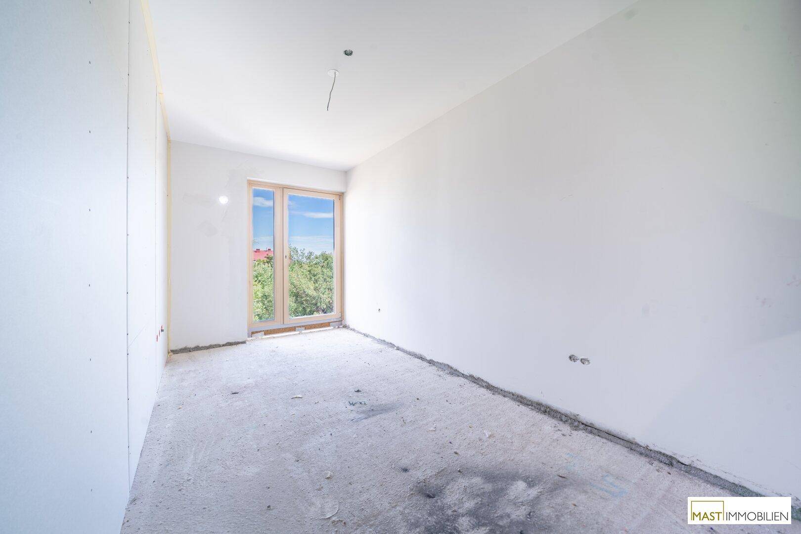 Weiteres unfertiges Schlafzimmer mit hellen Wänden, Betonboden und Fenster, das auf die Fertigstellung wartet.