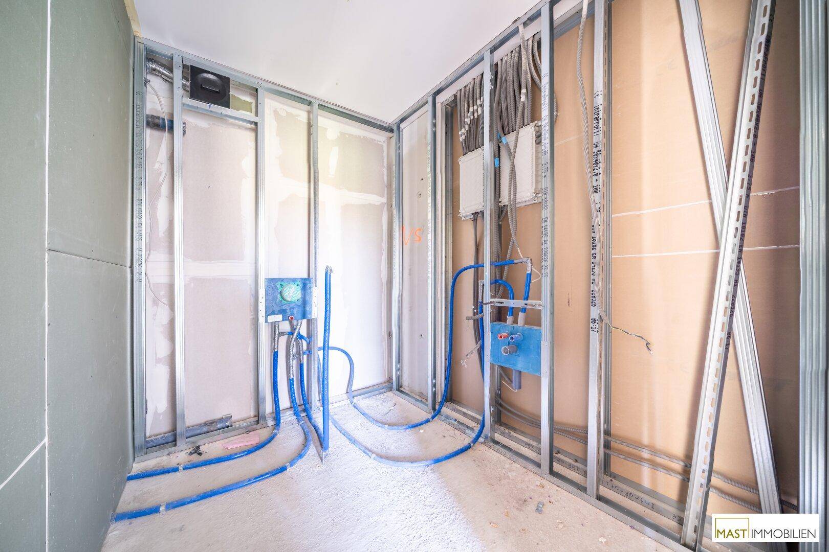 Kleiner Badezimmer-Rohbau mit zahlreichen Wasserleitungen und Elektrokabeln, bereit für die Sanitärmontage.