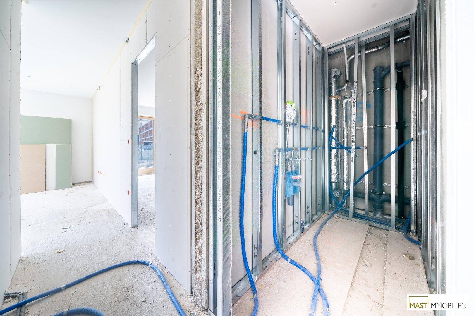 Bereich im Rohbau mit umfangreichen Rohrinstallationen und Metallständerwerk, wahrscheinlich für ein Badezimmer.