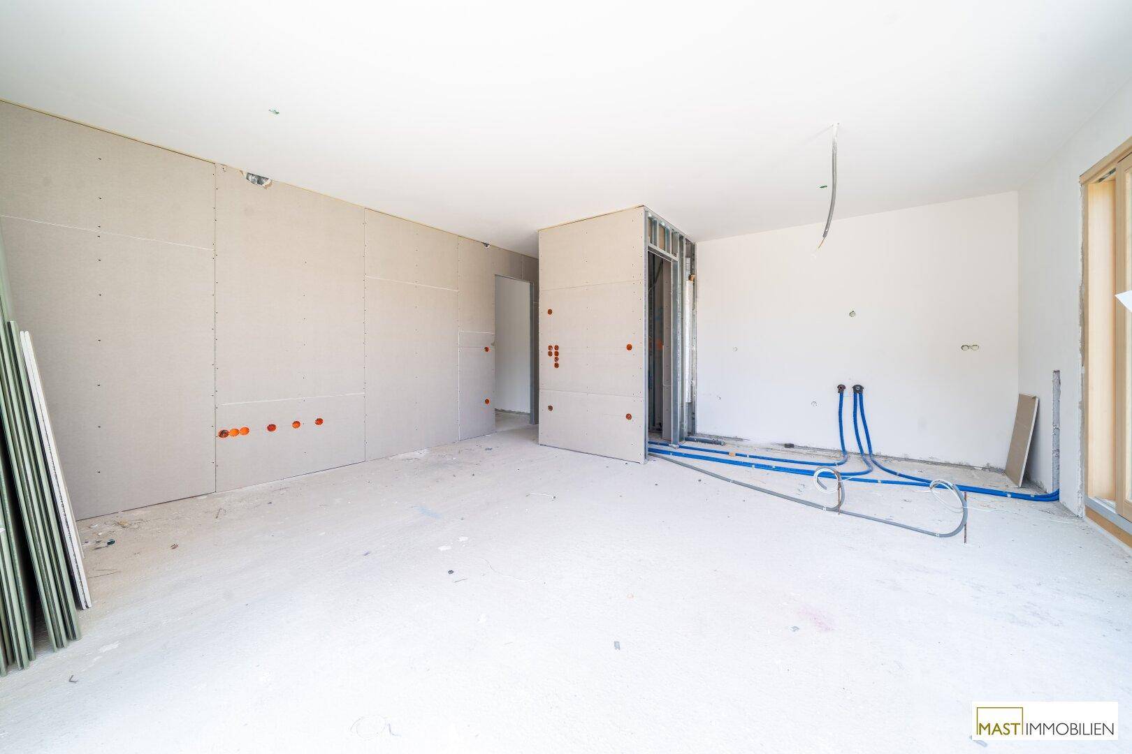 Unfertiger Innenraum im Rohbau mit Trockenbauwänden und sichtbaren Installationen für den weiteren Ausbau.