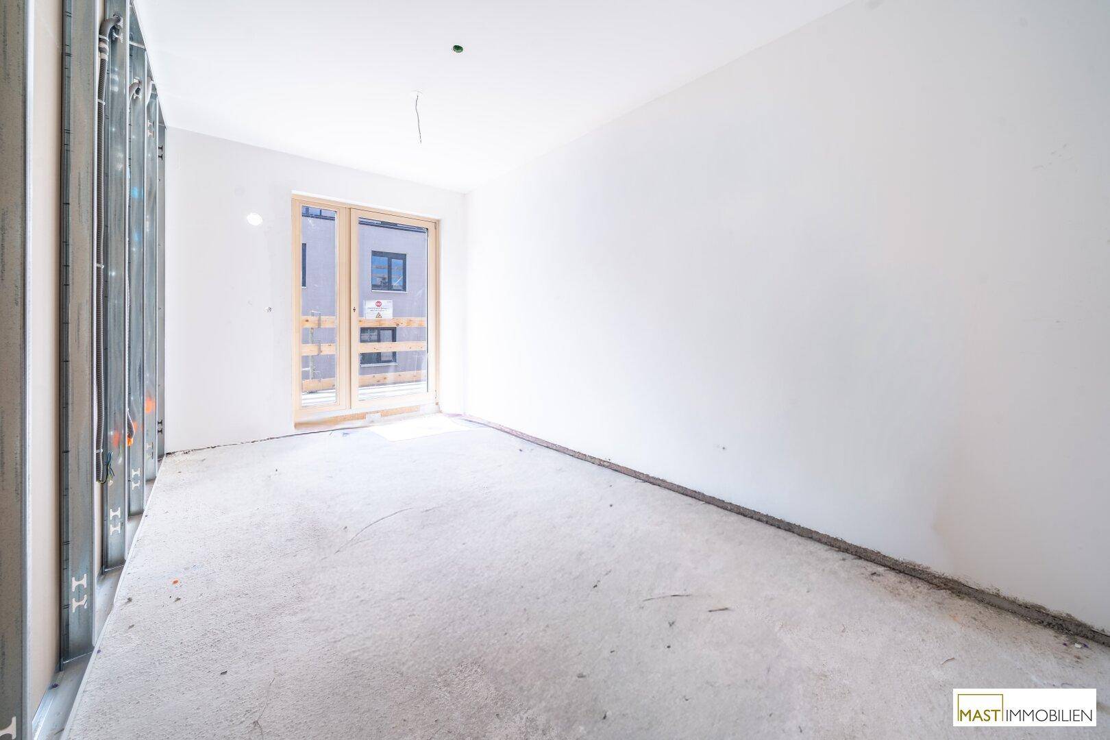 Heller Rohbau-Raum mit Betonboden und einem großen Fenster, bereit für den Innenausbau.