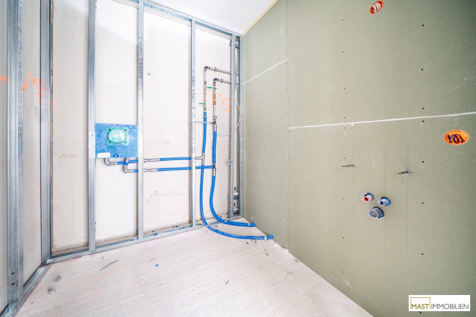 Rohbau-Badezimmer mit sichtbaren Wasserleitungen und vorbereiteten Wänden für die Installation.