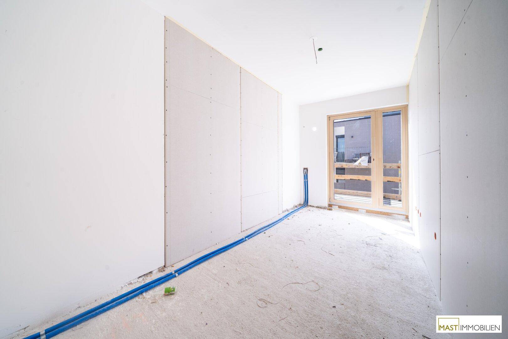 Rohbau-Raum mit Trockenbauwänden und sichtbaren blauen Leitungen, bereit für weitere Installationen.