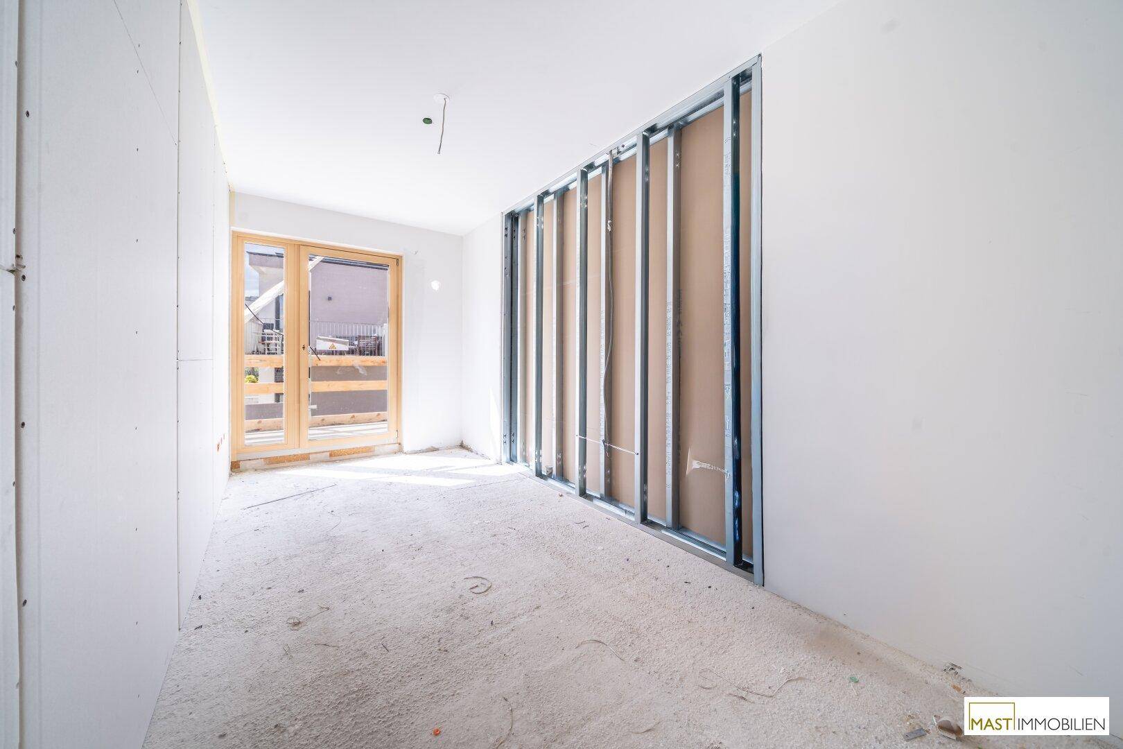Unfertiger Innenraum mit Metallständern für Wände und einem großen Fenster, viel Tageslicht.
