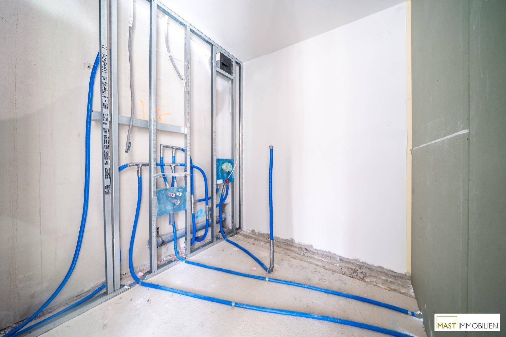 Rohbau-Badezimmer mit umfangreichen Wasserinstallationen und vorbereiteten Wänden für den Ausbau.