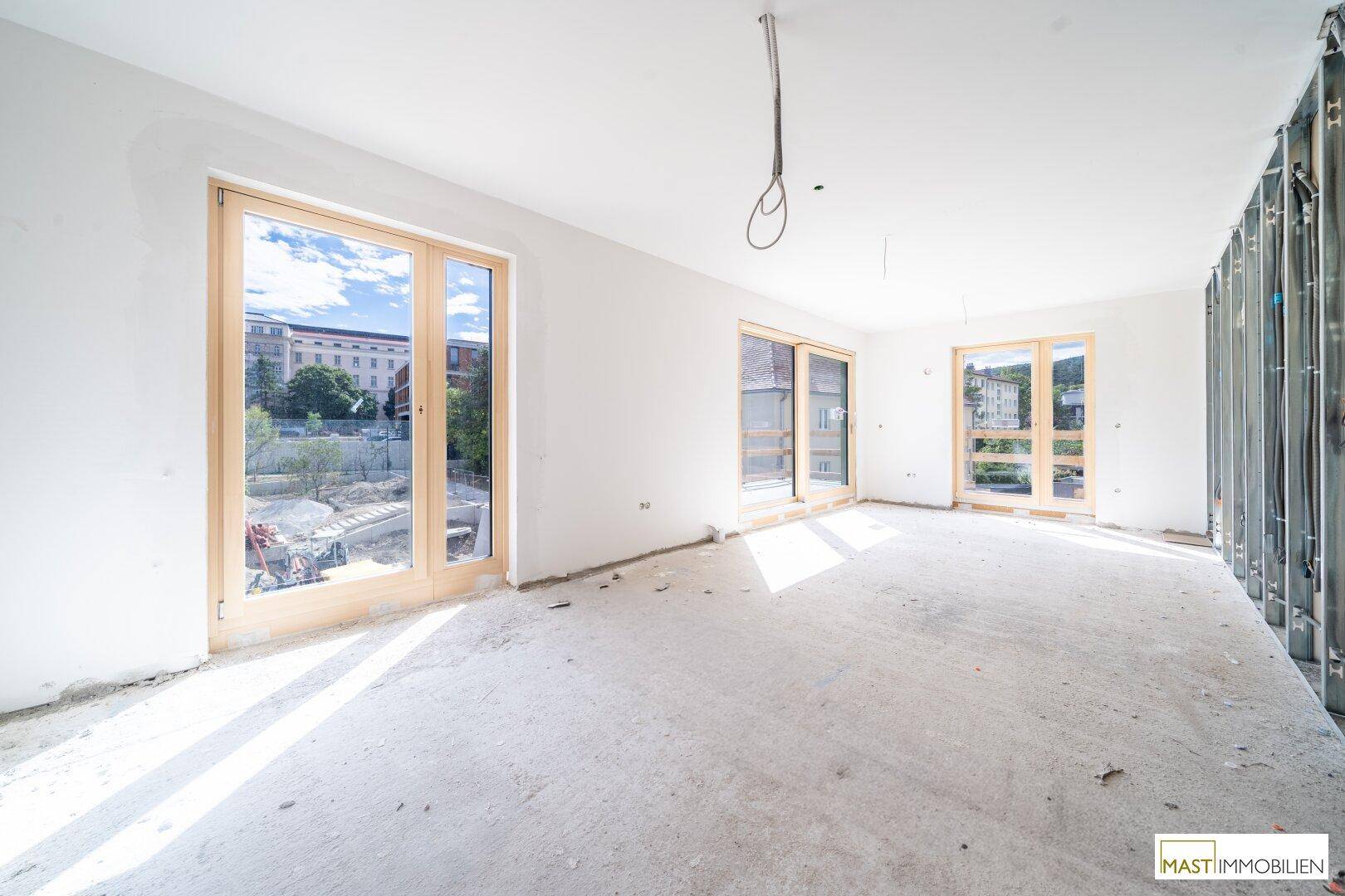 Unfertiger Innenraum mit Betonboden und großen Holzfenstern, bereit für den Ausbau.
