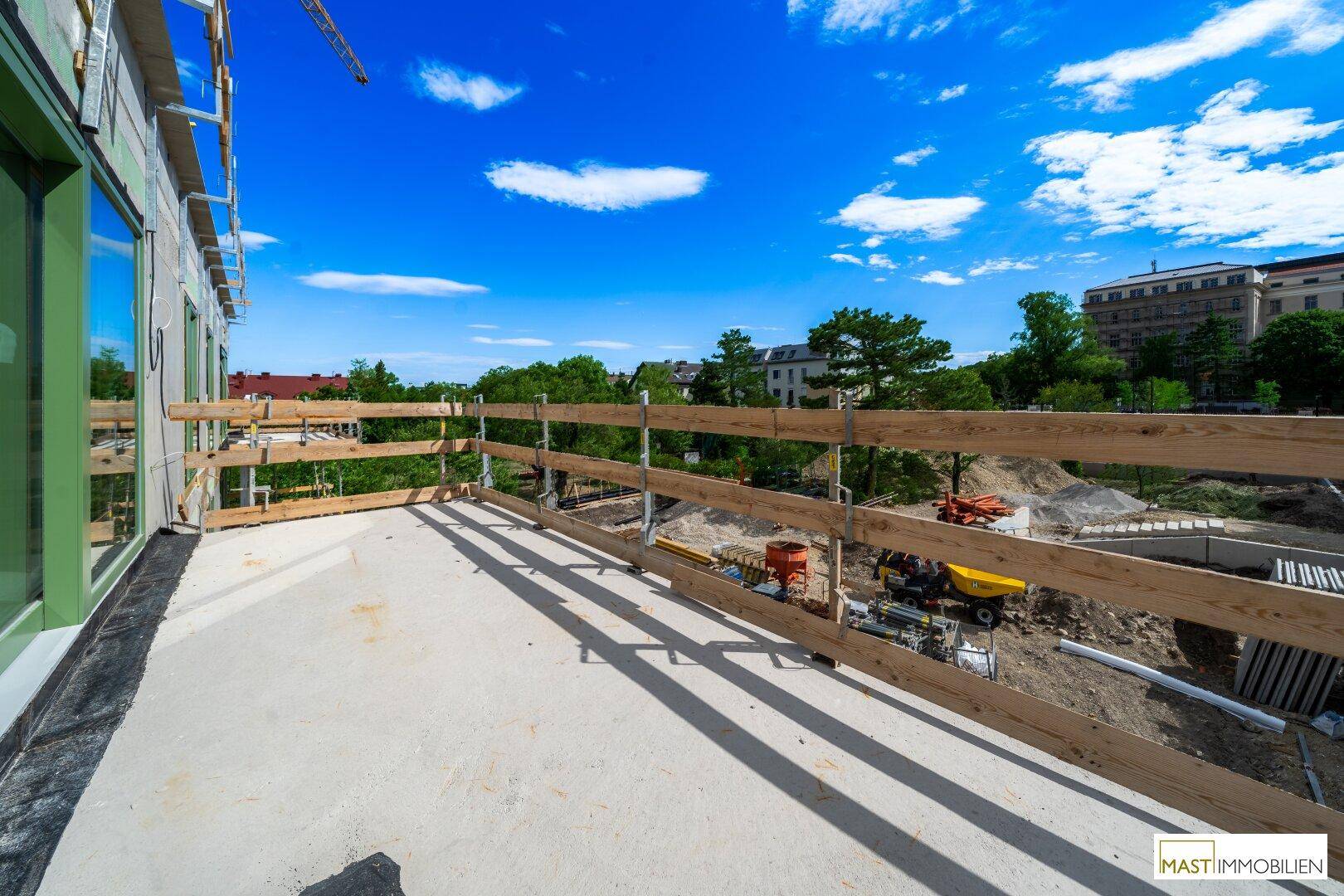 Unfertige Terrasse mit Holzzaun und Blick auf die Baustelle und die umliegende Landschaft.