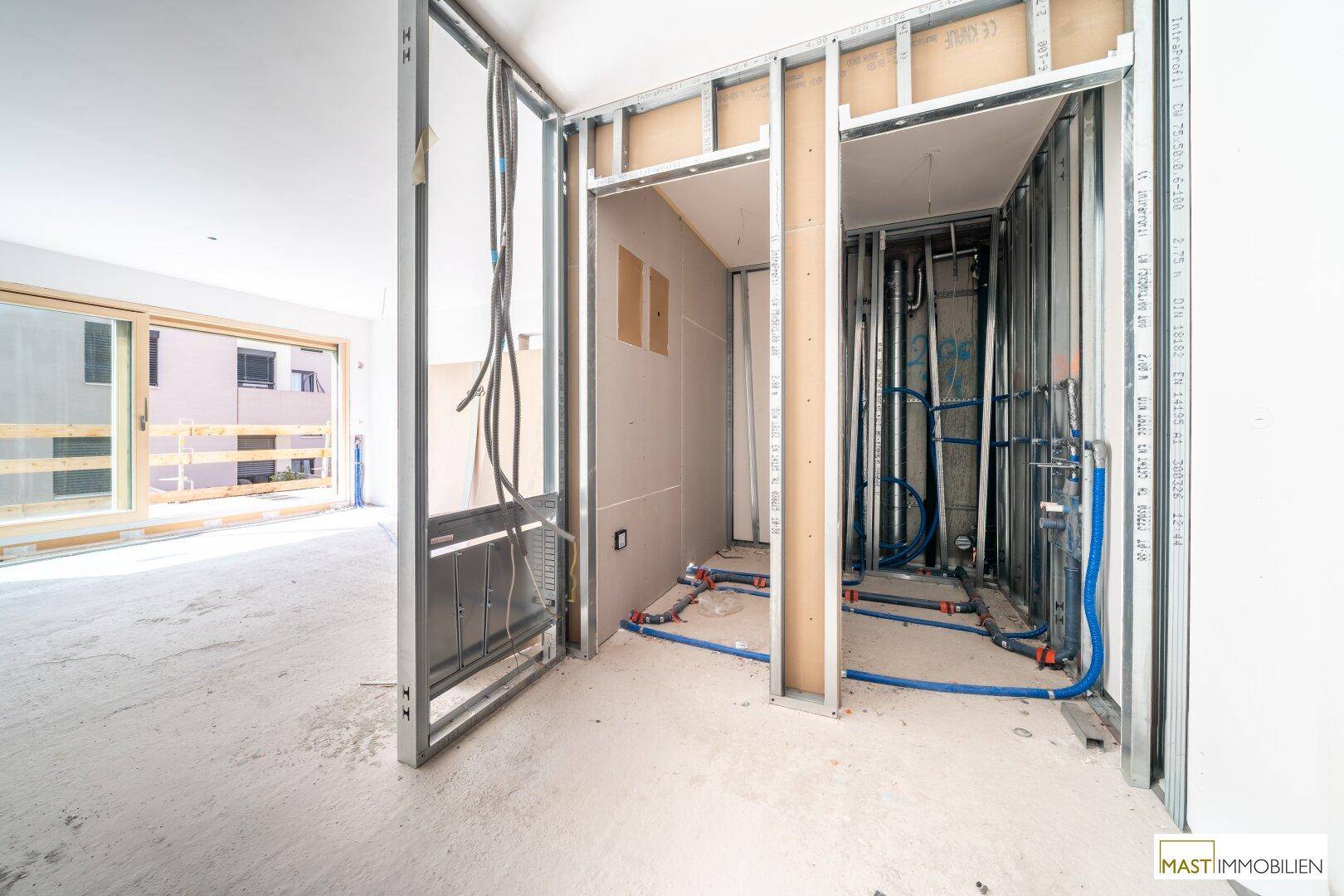 Baustelle im Innenbereich mit sichtbaren Rohrleitungen und Metallrahmen für zukünftige Wände.