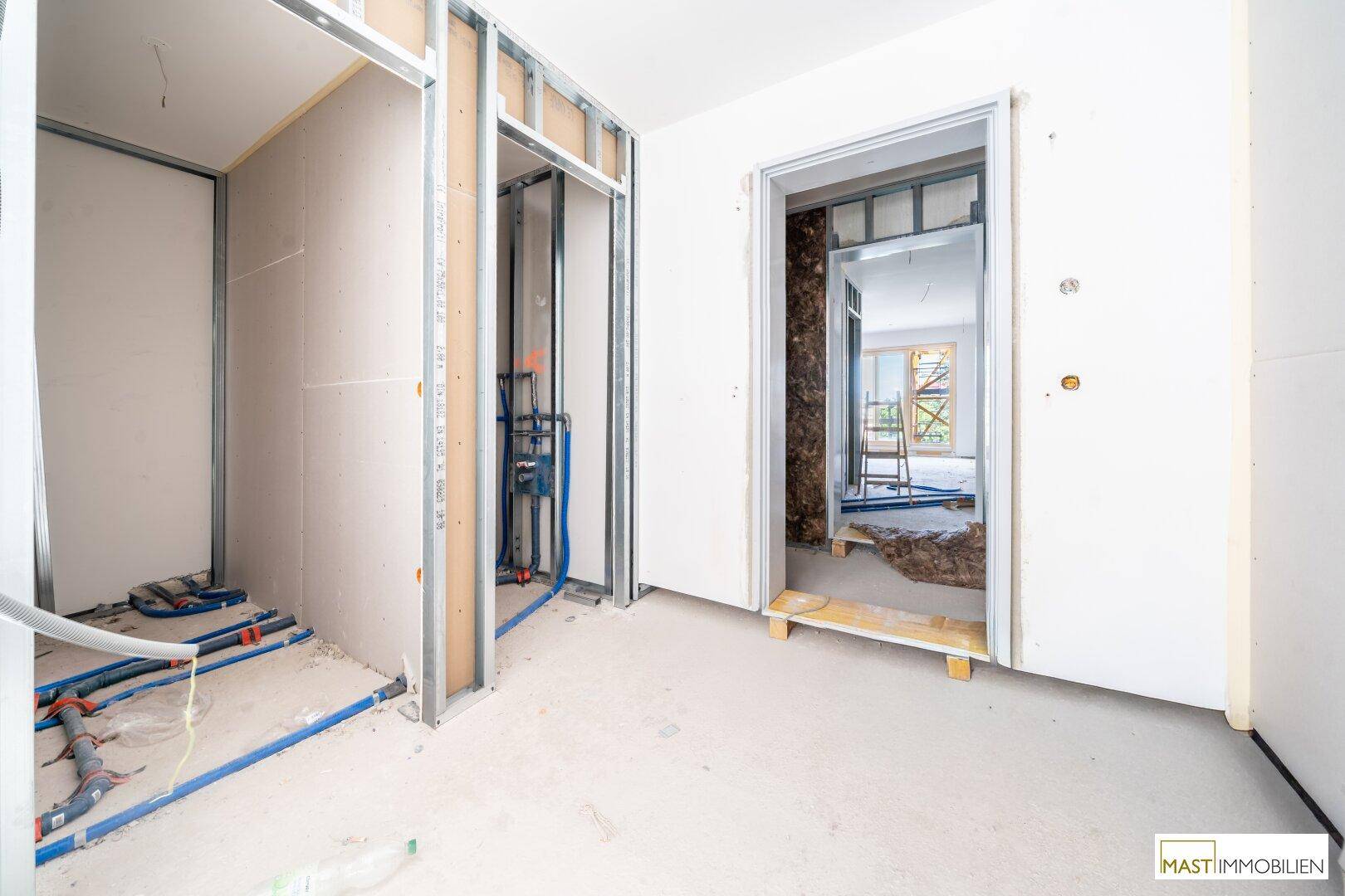 Rohbau eines Innenraums mit sichtbaren Installationen und Metallständerwerk für Wände.
