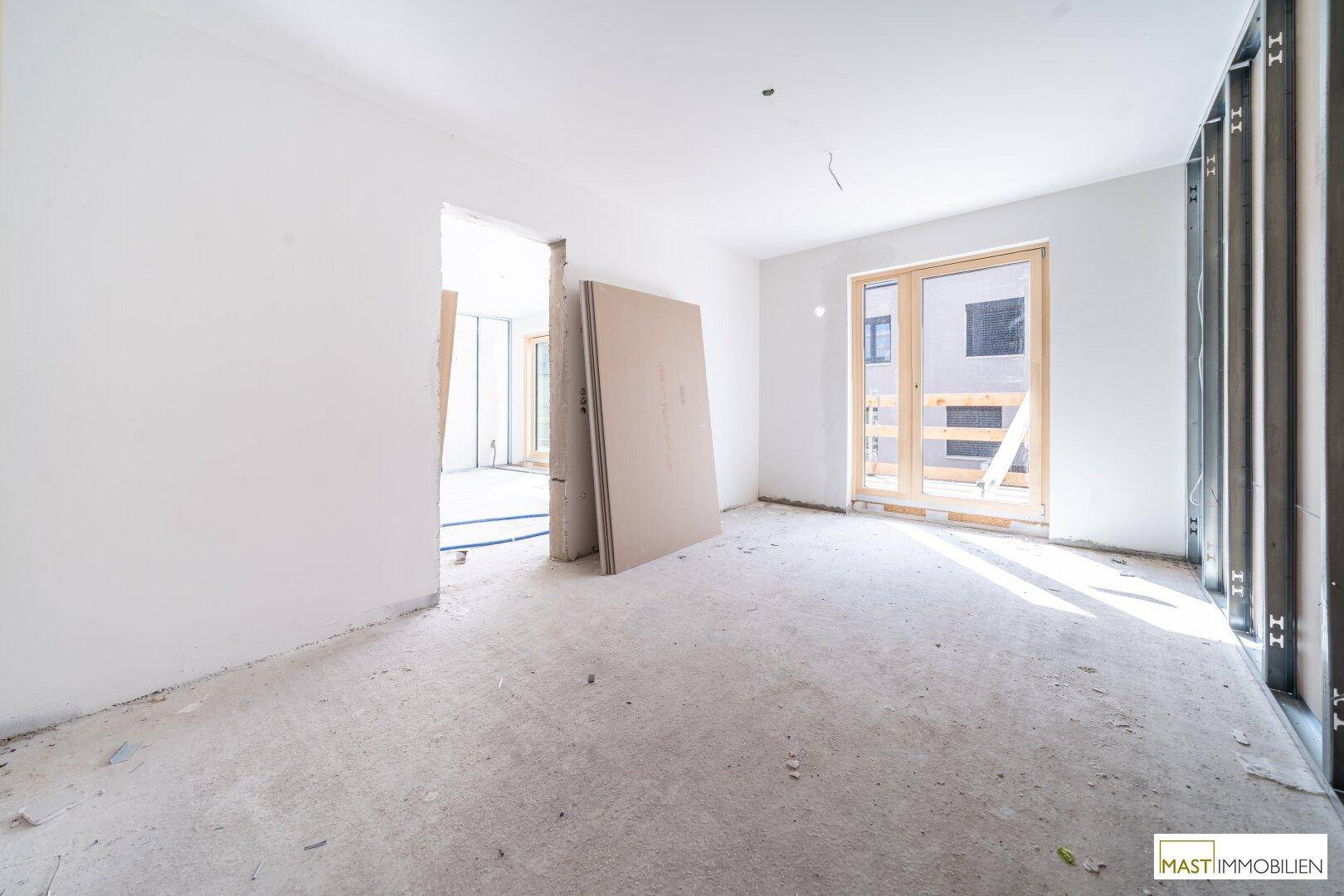 Unfertiger Innenraum mit Rohbauelementen und Tageslichteinfall durch die Fenster.
