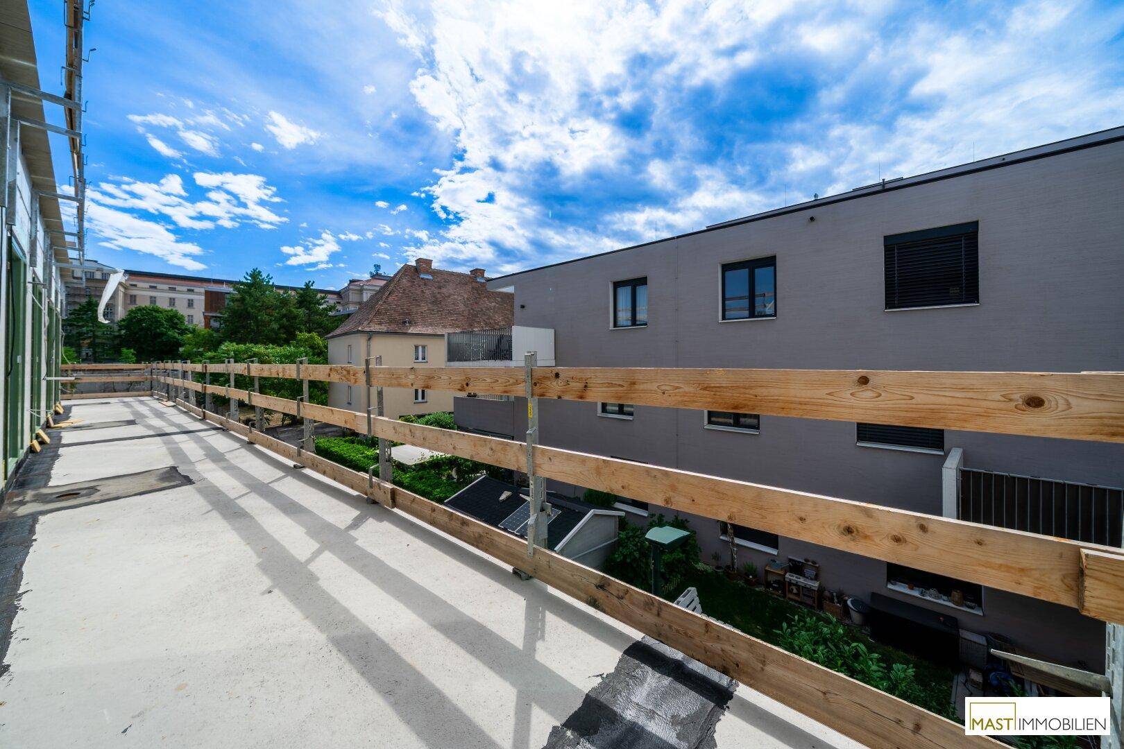 Unfertiger Balkon mit Holzgeländer und Blick auf angrenzende Gebäude.