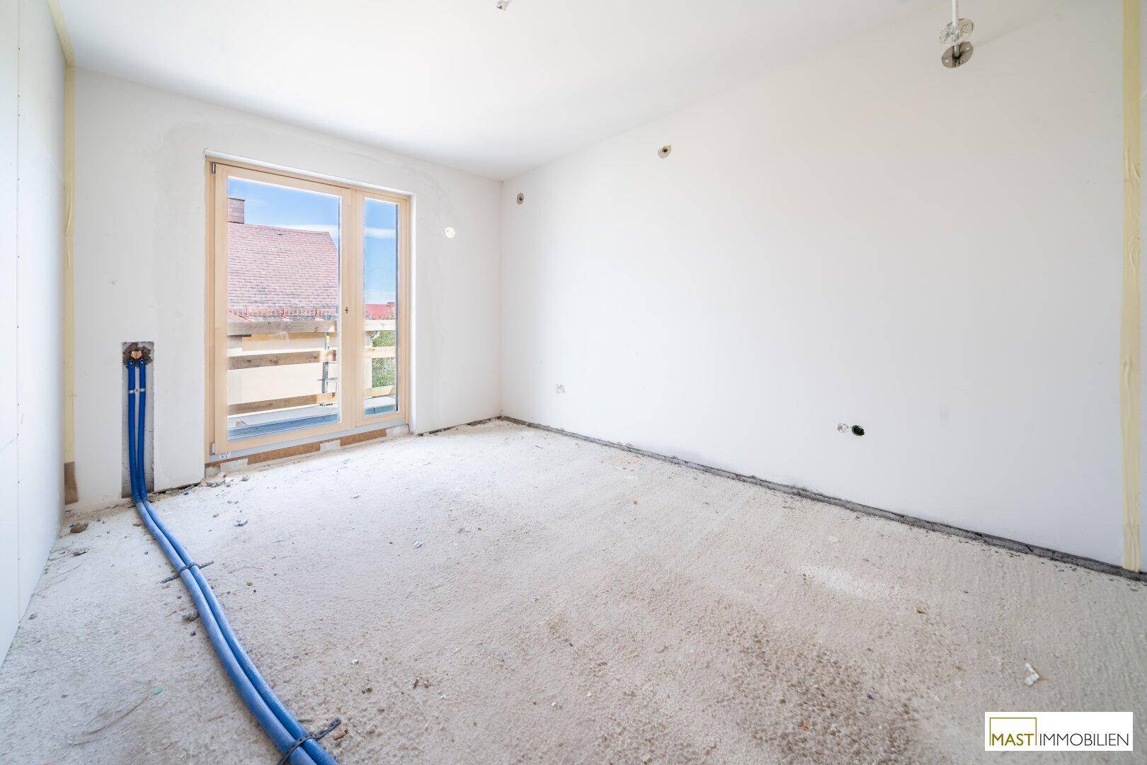 Unfertiger Raum mit Zugang zu einem potenziellen Balkon oder einer Terrasse, mit sichtbaren Rohrleitungen.