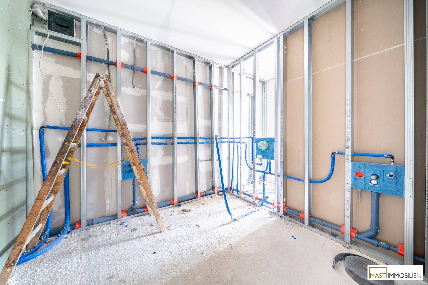 Rohbau-Raum mit sichtbaren Metallständerwänden und komplexen Sanitärinstallationen, bereit für die Fertigstellung.