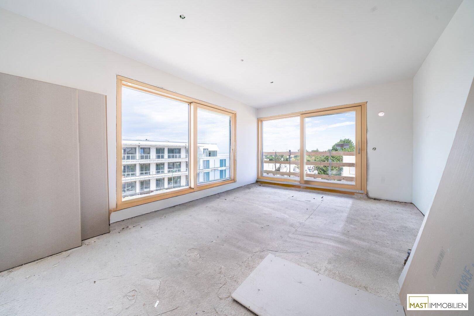 Heller Rohbau-Raum mit großen Fenstern und Blick auf umliegende Gebäude, bereit für den Innenausbau.